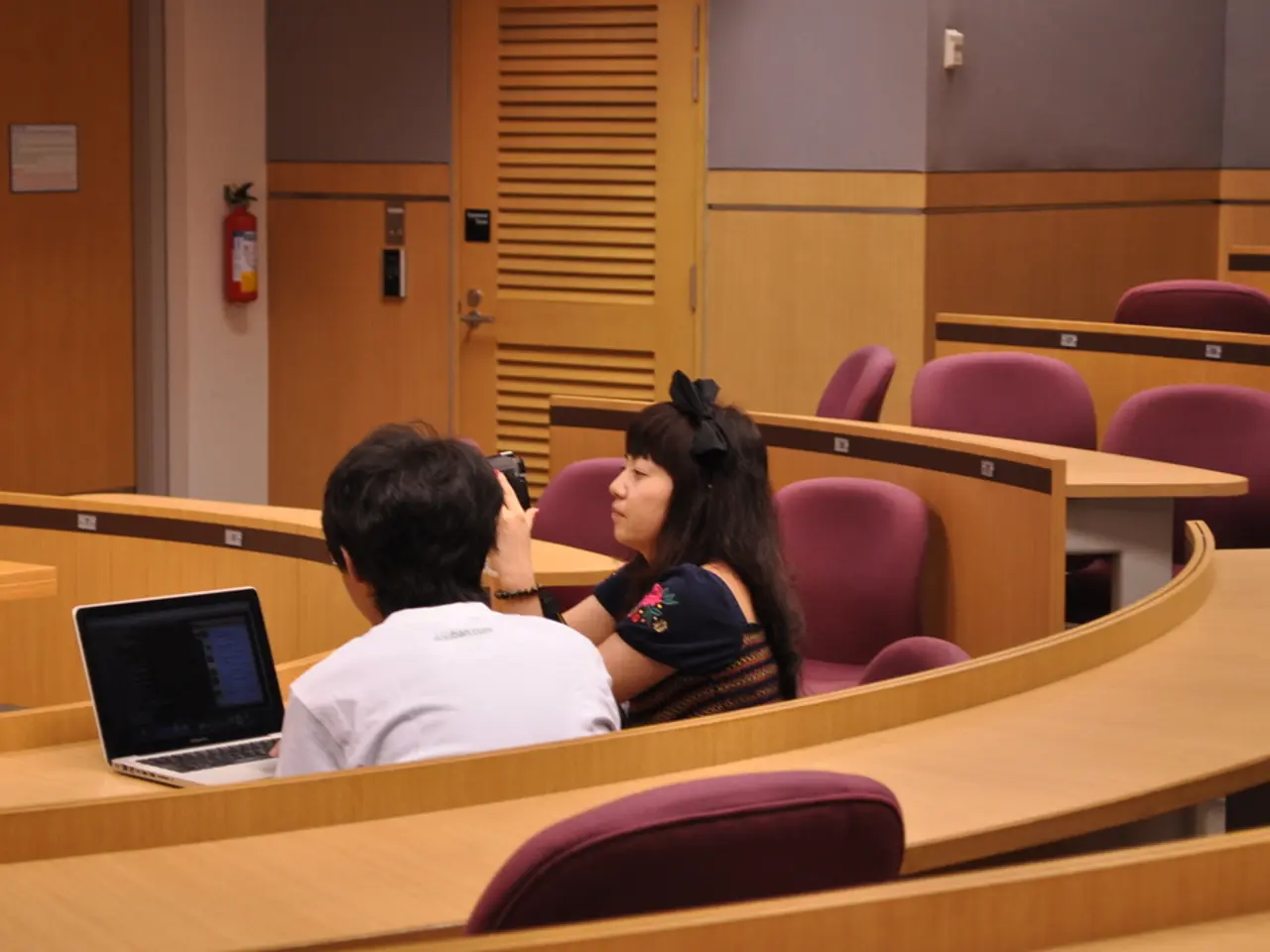 This picture is taken in a conference hall where two persons are sitting on a chair. The woman in...