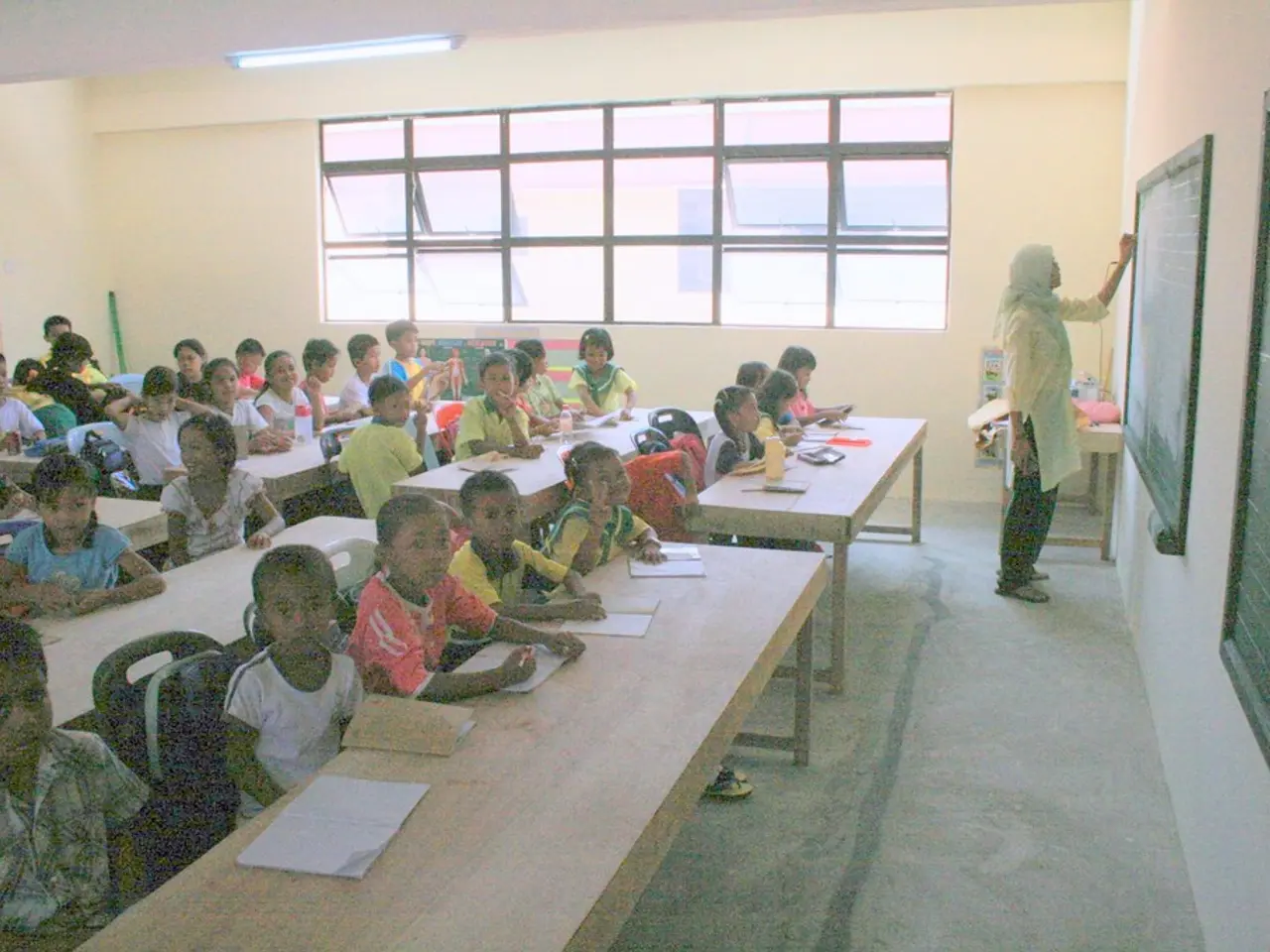 This Image is clicked in a classroom where there is a blackboard on the right side and women is...