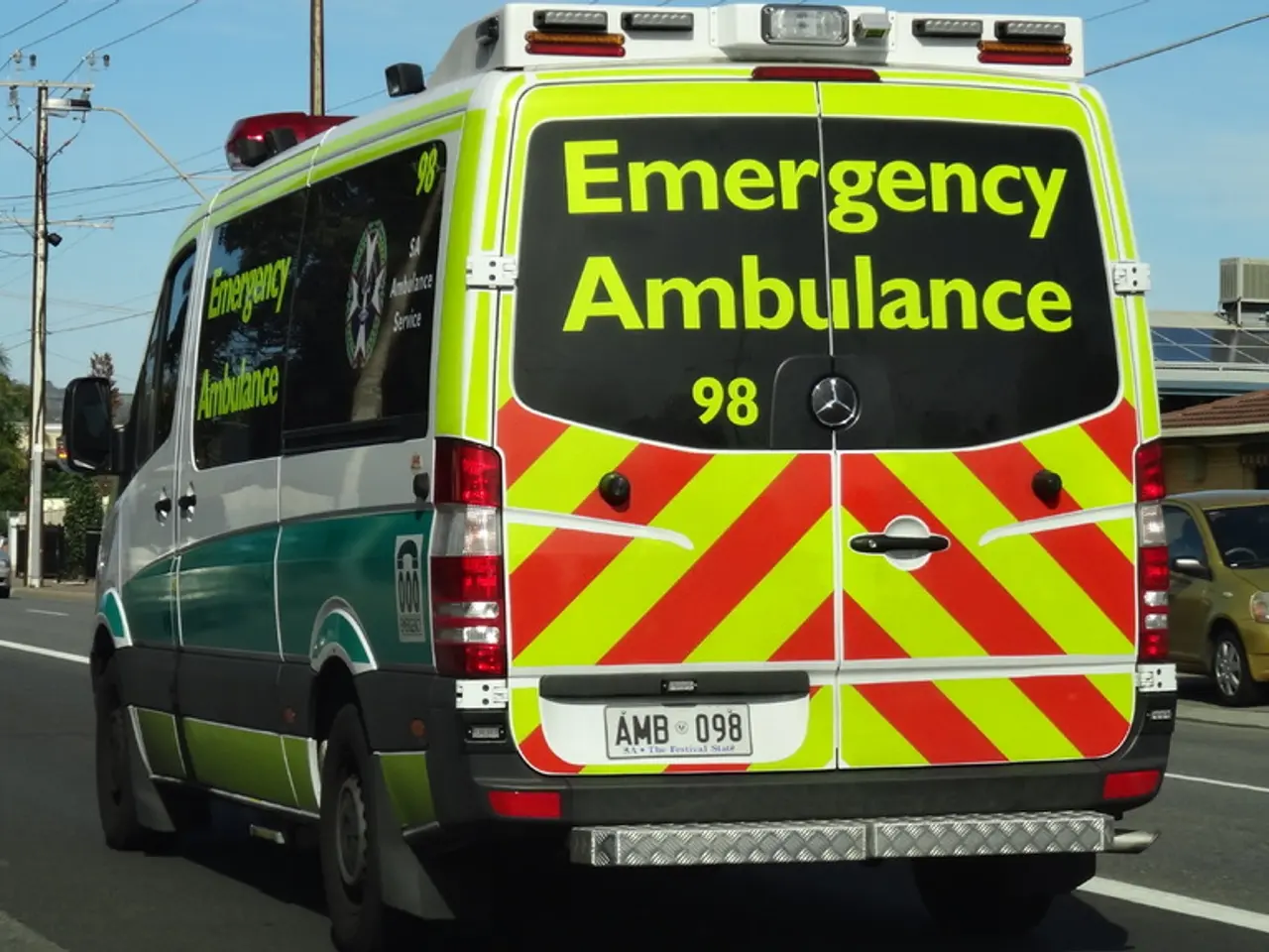 Vehicles are on the road. Background there are trees, solar panel, current poles with cables and...