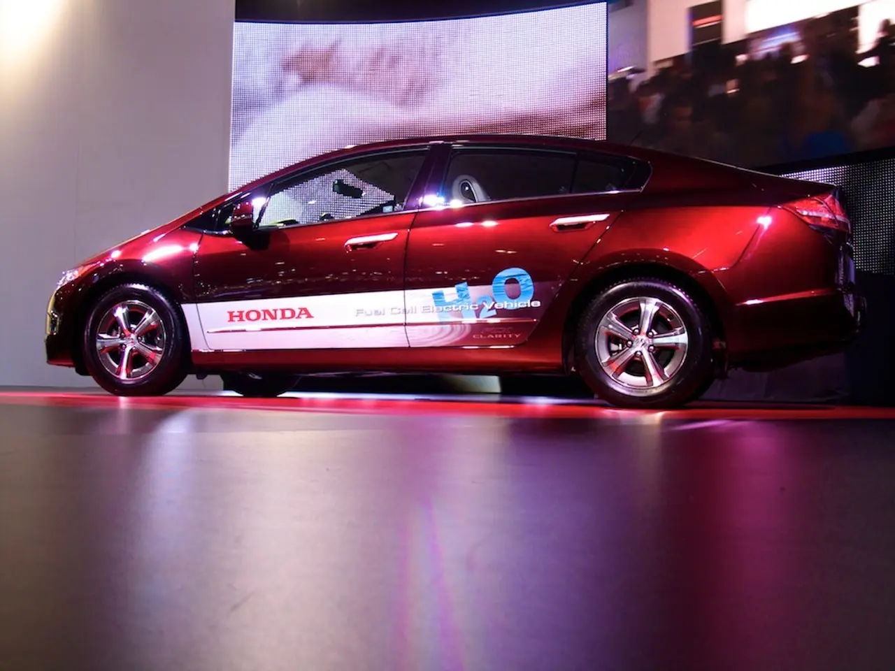 In this picture I can see a red car, and in the background there are screens.