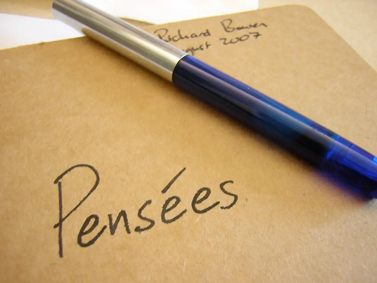 In this picture we can see a writing pad in the front, there is some text and a pen present on this...