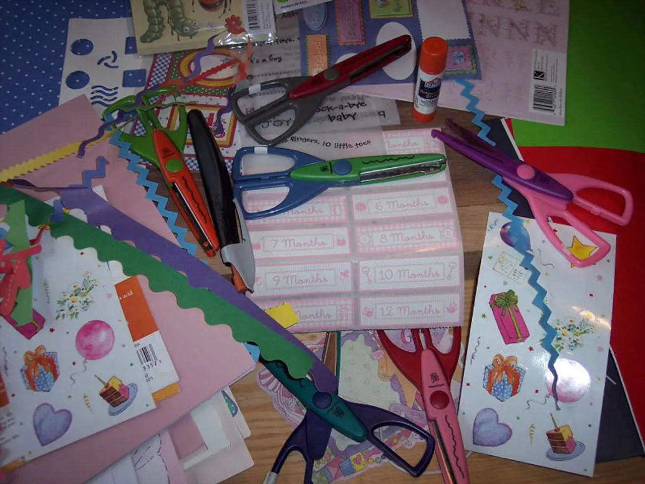 This picture shows few papers and few scissors and a glue stick and few color papers on the table.