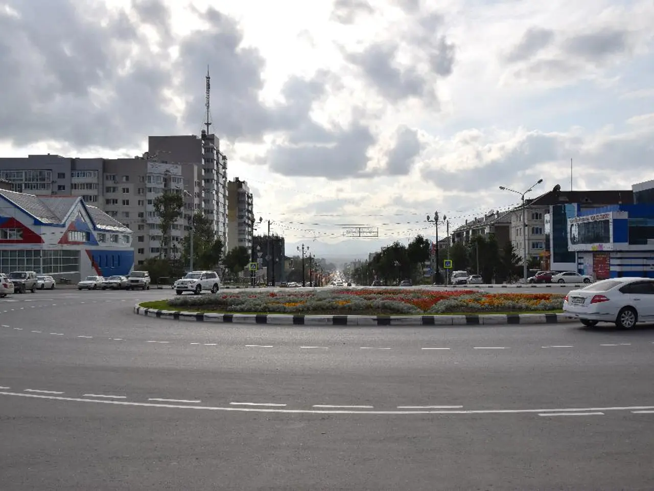 At the top of the image we can see sky with clouds, buildings, towers, trees, street poles, street...