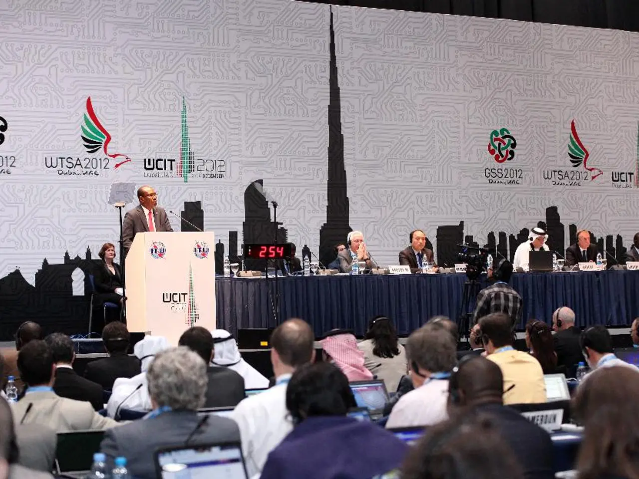 In this image we can see a few people, some of them are sitting, in front of them are few laptops,...