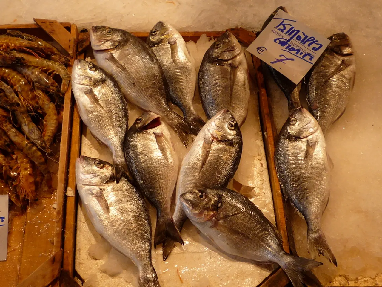 In this picture we can see there are fishes, shrimps on the wooden trays. On the right side of the...