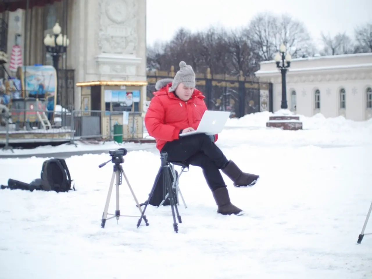In the center of the image a person is sitting on a chair and wearing hoodie and holding laptop. In...
