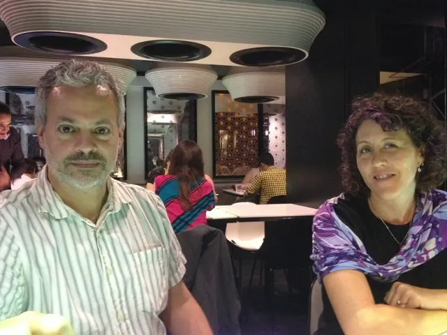 There are two people sitting on a chair and there are few other people sitting behind them.