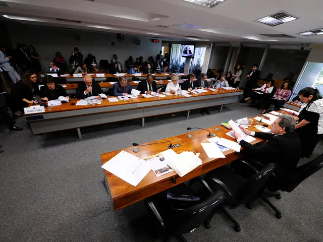 In this image I can see number of people where few of them are sitting on chairs and few are...