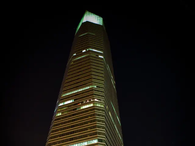 In this image there is a tall building. There are lights at the top of the building.